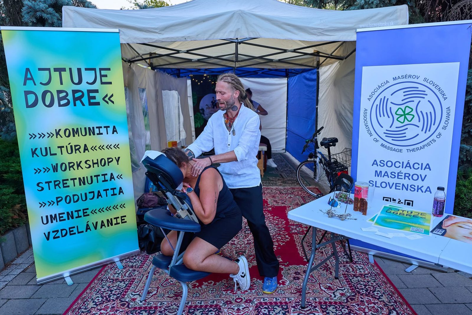 Masér Združenia masérov pracuje na masážnej stoličke pod stanom združenia na verejnom podujatí