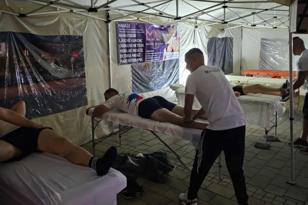 Tri masážne stoly obsadené naraz vo večerných hodinách, masér pracuje s bežcom po pretekoch